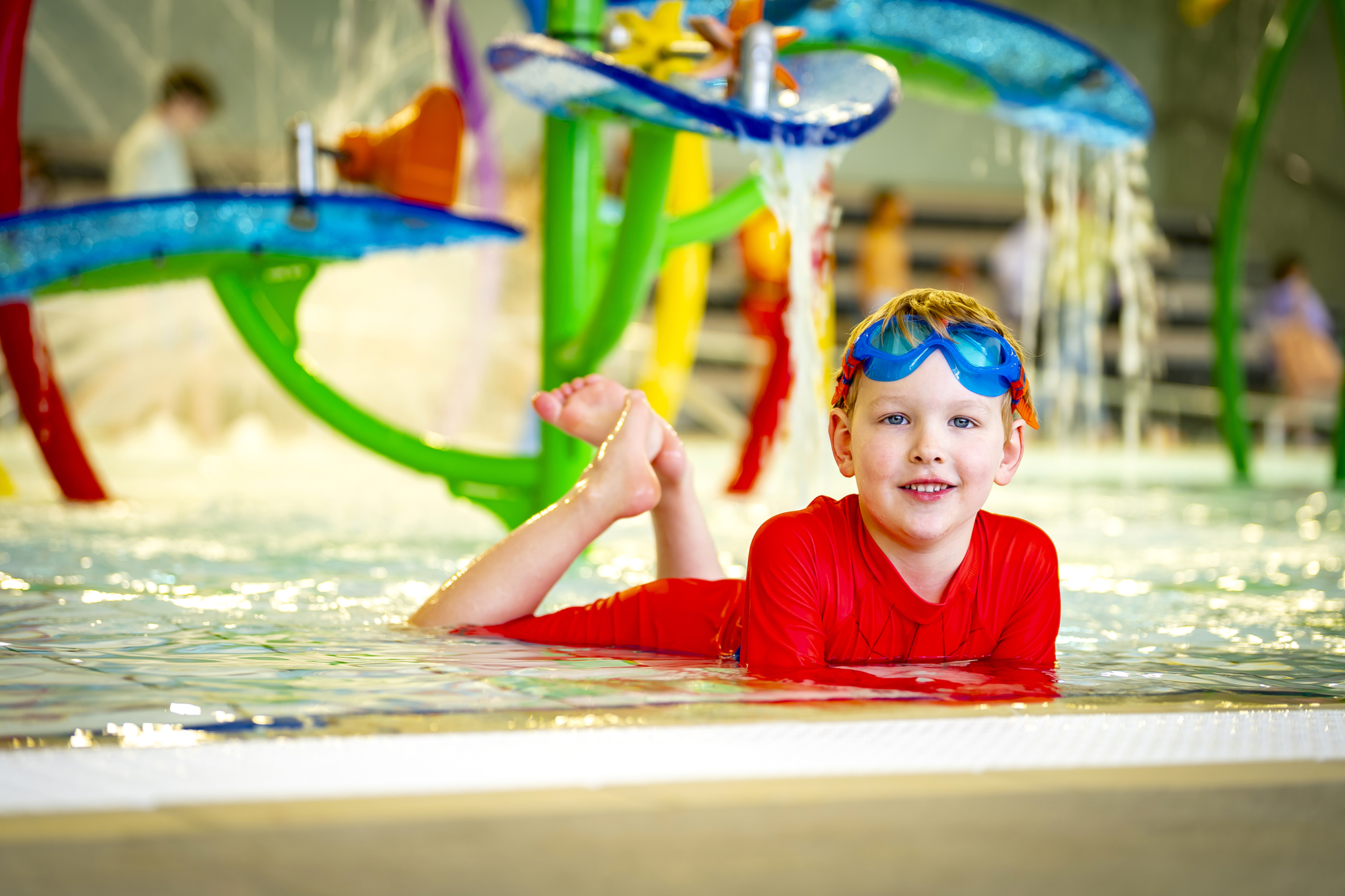 Child lies in the shallow water of the water play area